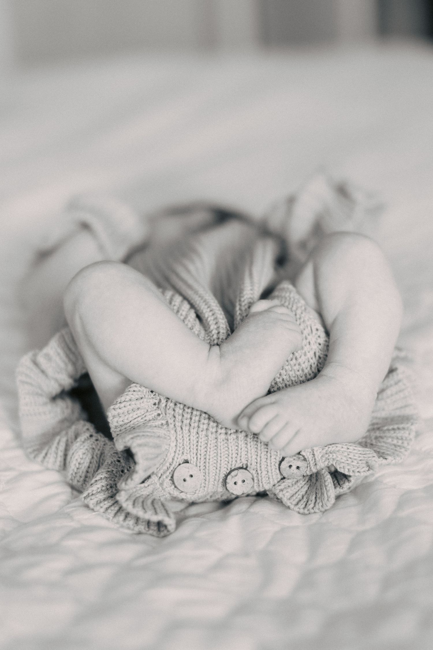 Black and white photo of newborn baby feet and legs in a knit romper on a soft white blanket.