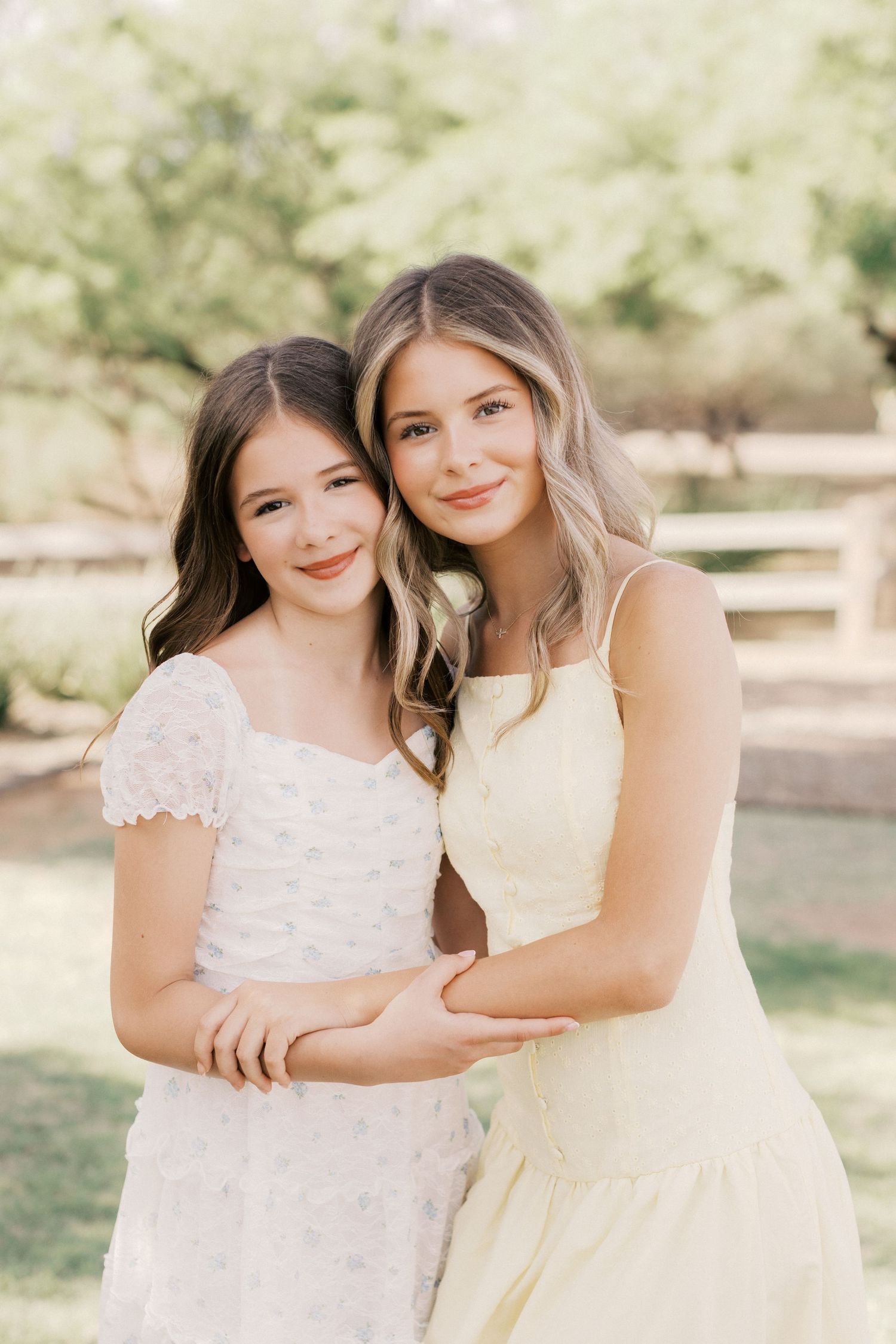 Two teenage girls smiling and embracing outdoors in summer dresses in garden.