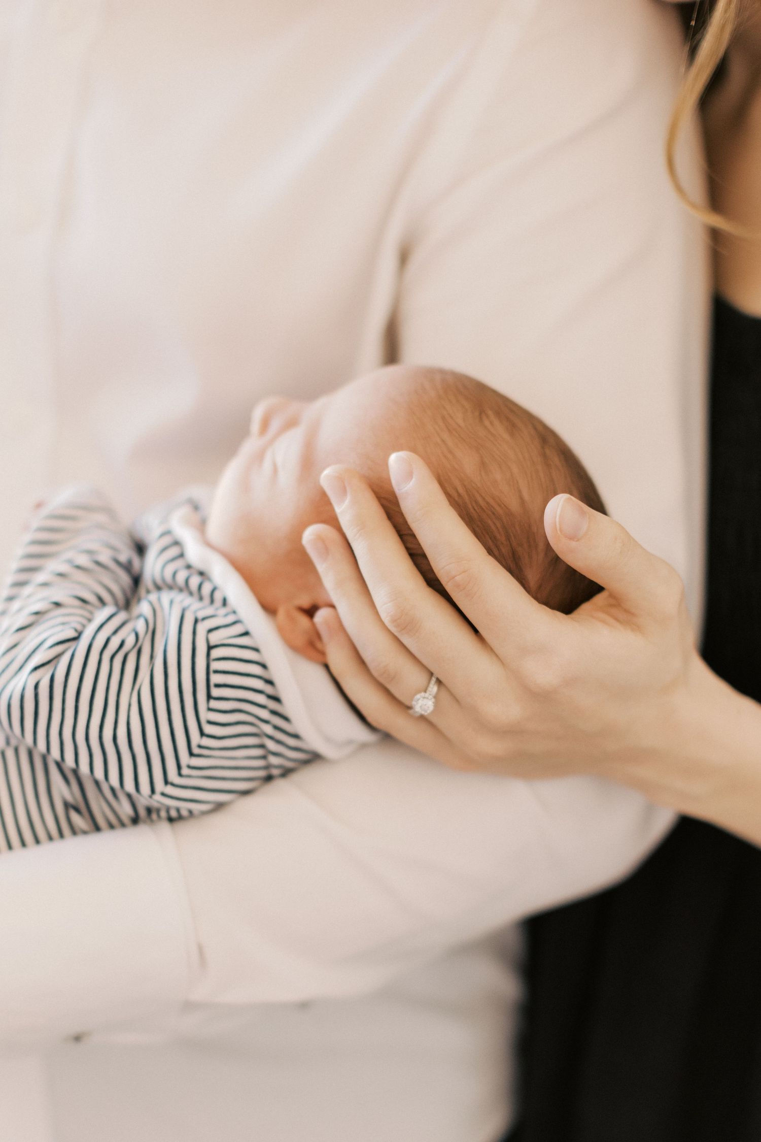 A mother cradling her newborn baby in a striped onesie, wearing a diamond ring, in a soft and tender embrace.