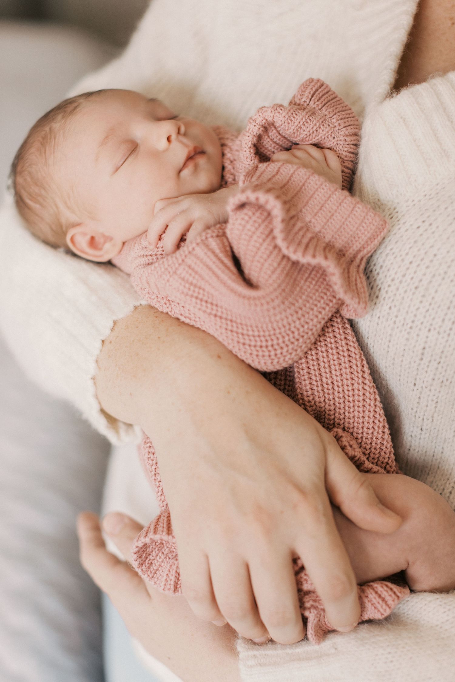 Newborn baby sleeping peacefully in parent's arms, dressed in a soft pink knit romper.