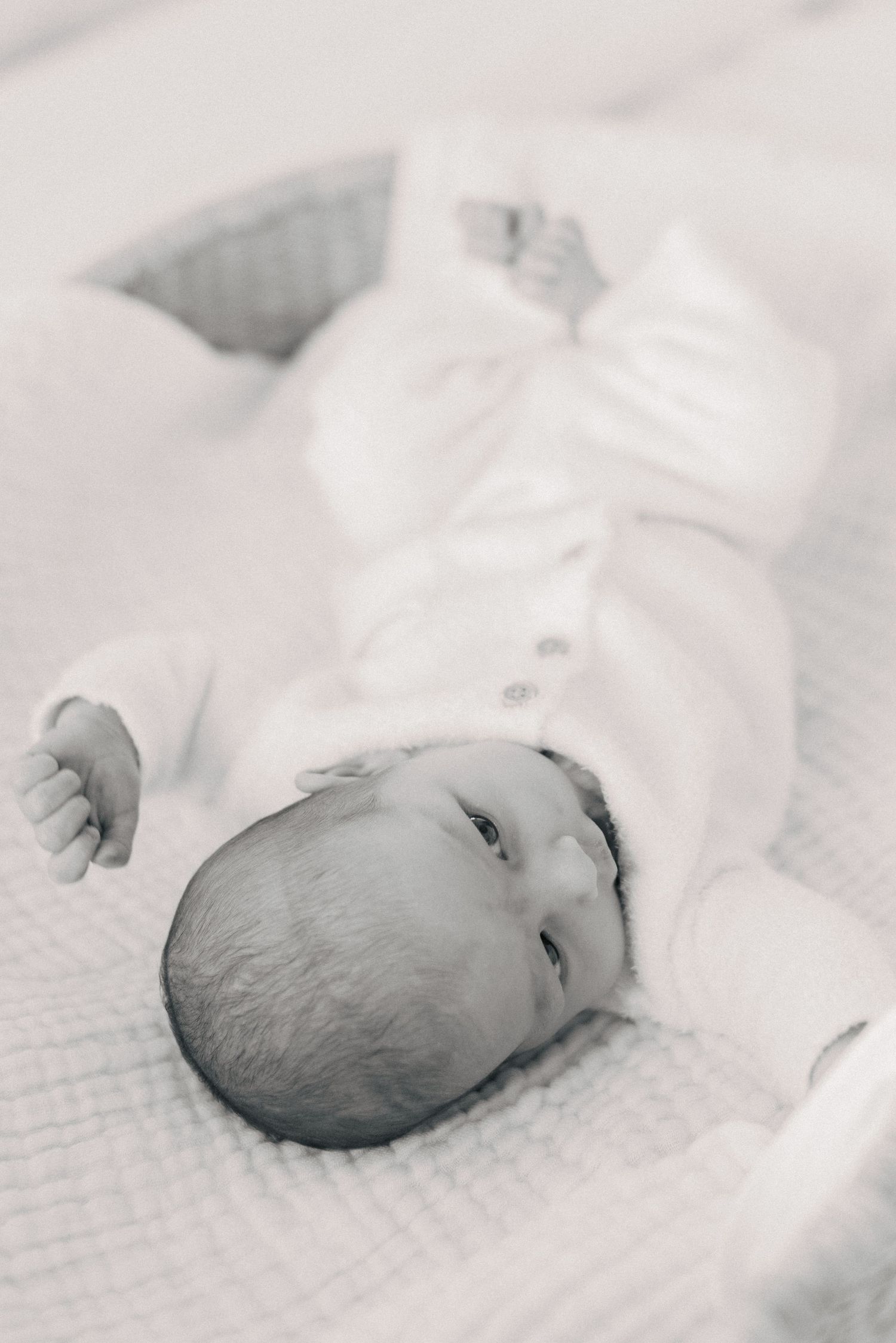 Black and white photo of a peaceful newborn baby lying on a soft white blanket in a cozy bassinet.
