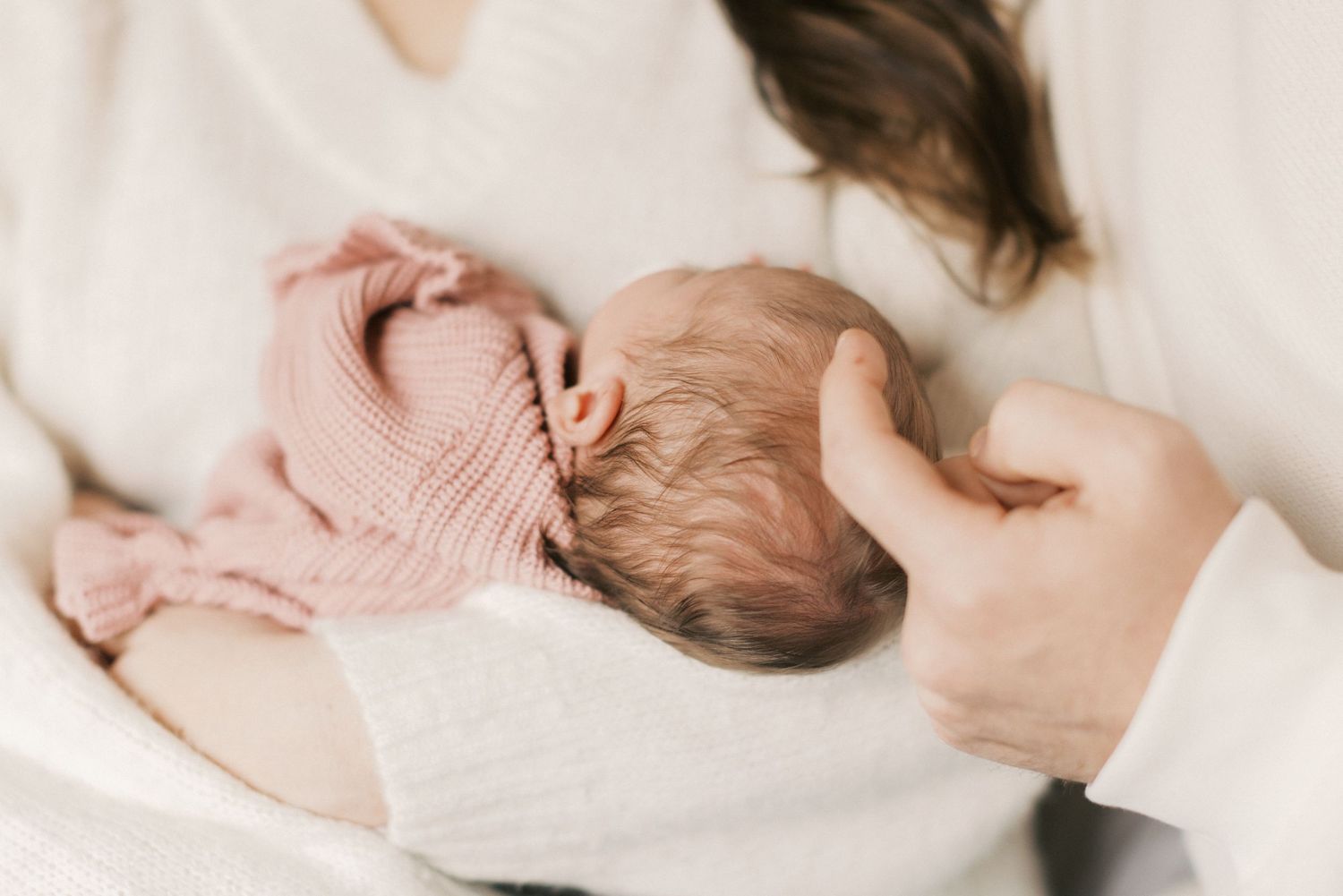 Mother cradling sleeping newborn baby wrapped in pink knit blanket, close-up photo.