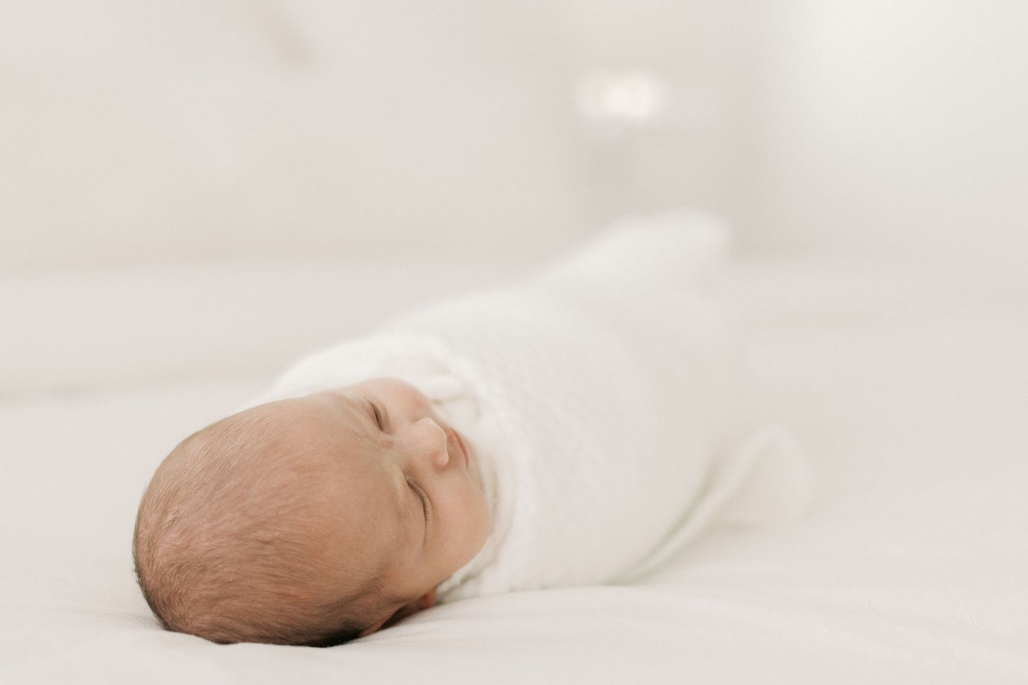 Peaceful newborn baby swaddled in white wrap sleeping on a soft white blanket.