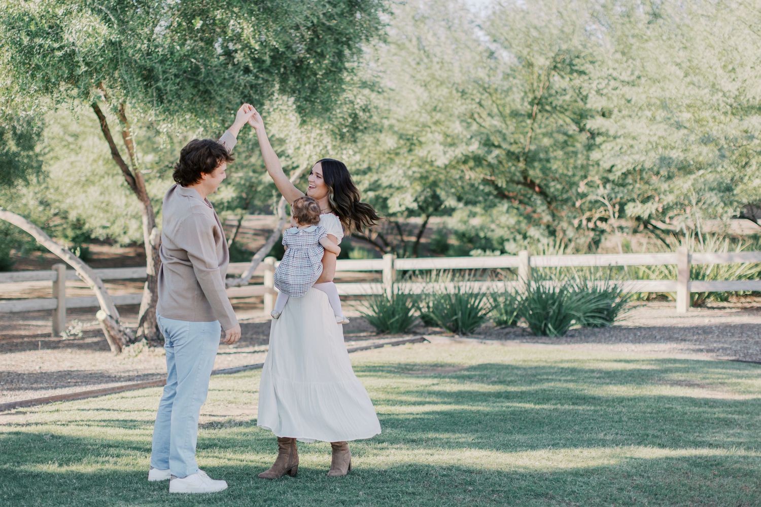 A couple dances outdoors in a lush green park, with a white fence and trees in the background.