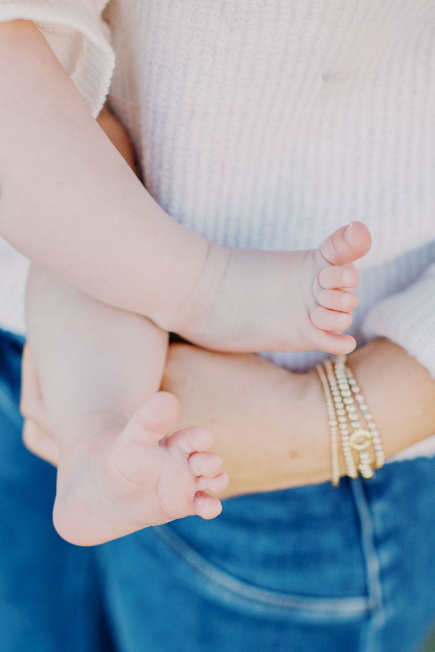 Artistic close-up photos of baby feet with delicate pearl bracelets against blue denim.