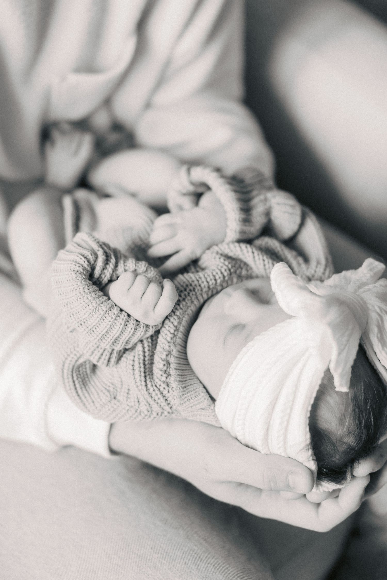 Black and white photo of a sleeping newborn baby in knit outfit cradled in mother's arms.