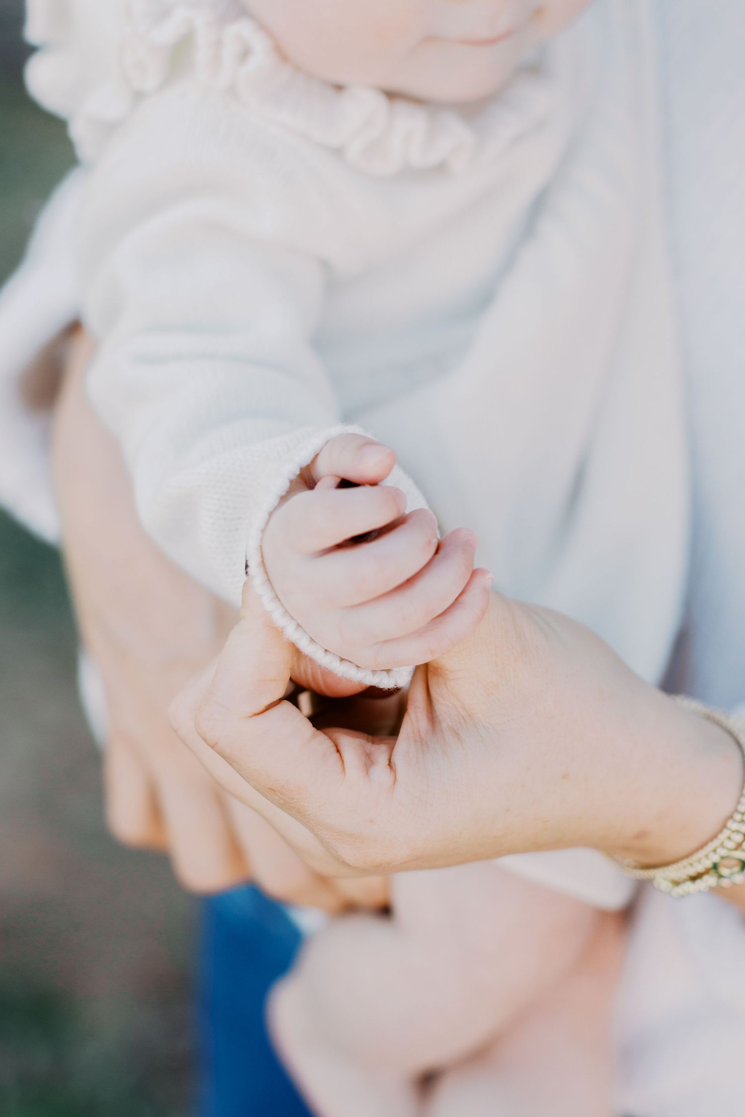 Close-up of tiny baby hand gripping parent's finger, wearing delicate bracelet in soft natural light.