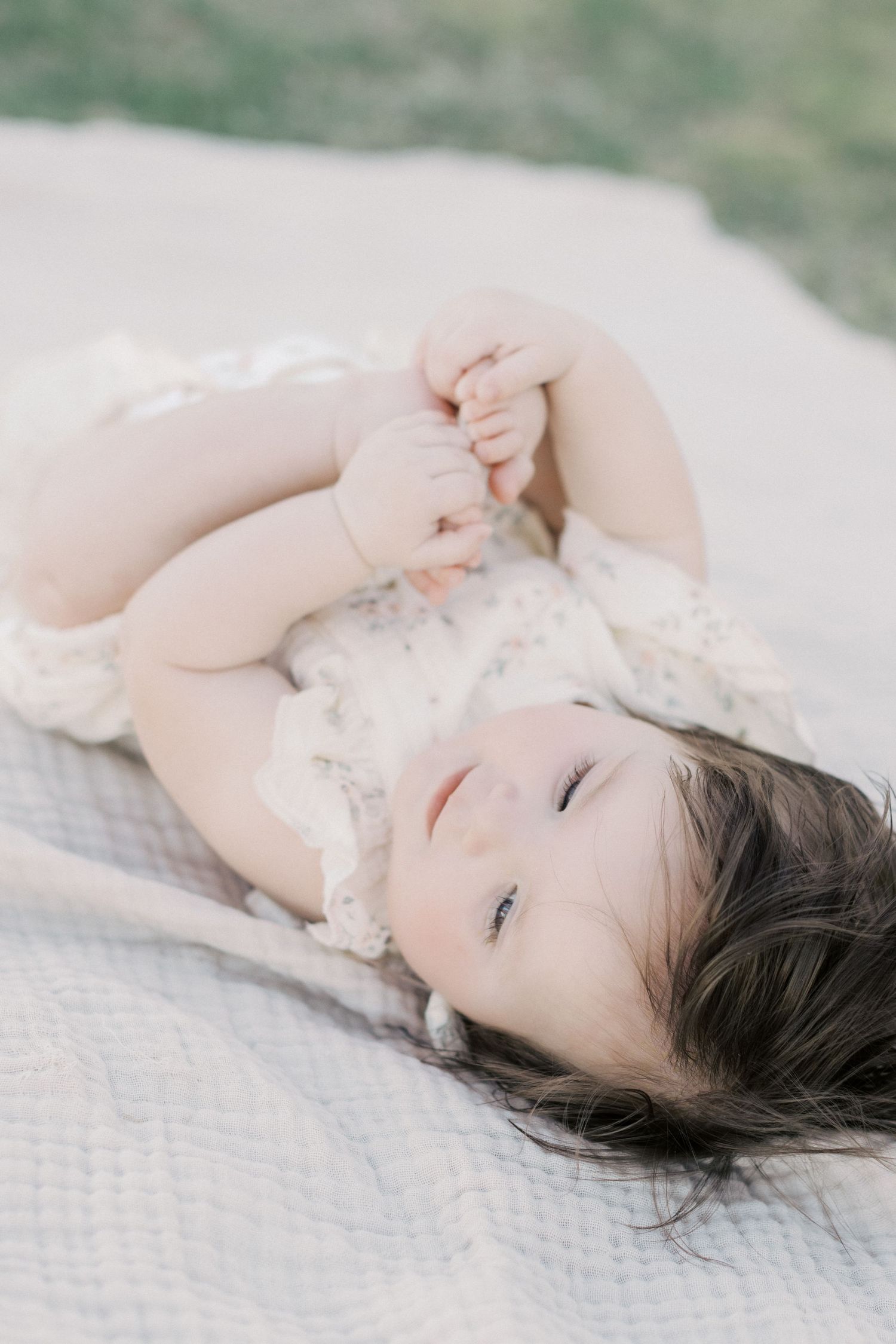 Adorable baby girl in floral romper lying on blanket looking up at camera.
