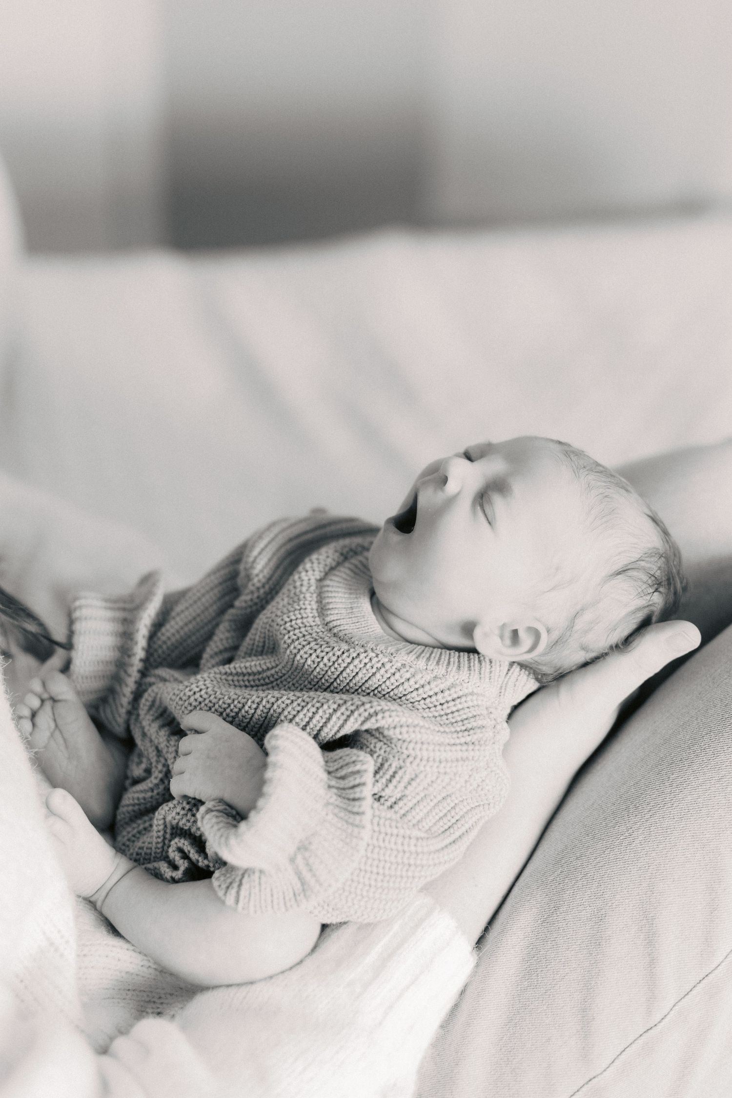 Sleeping newborn baby in knit sweater cradled in parent's arms, black and white photo.