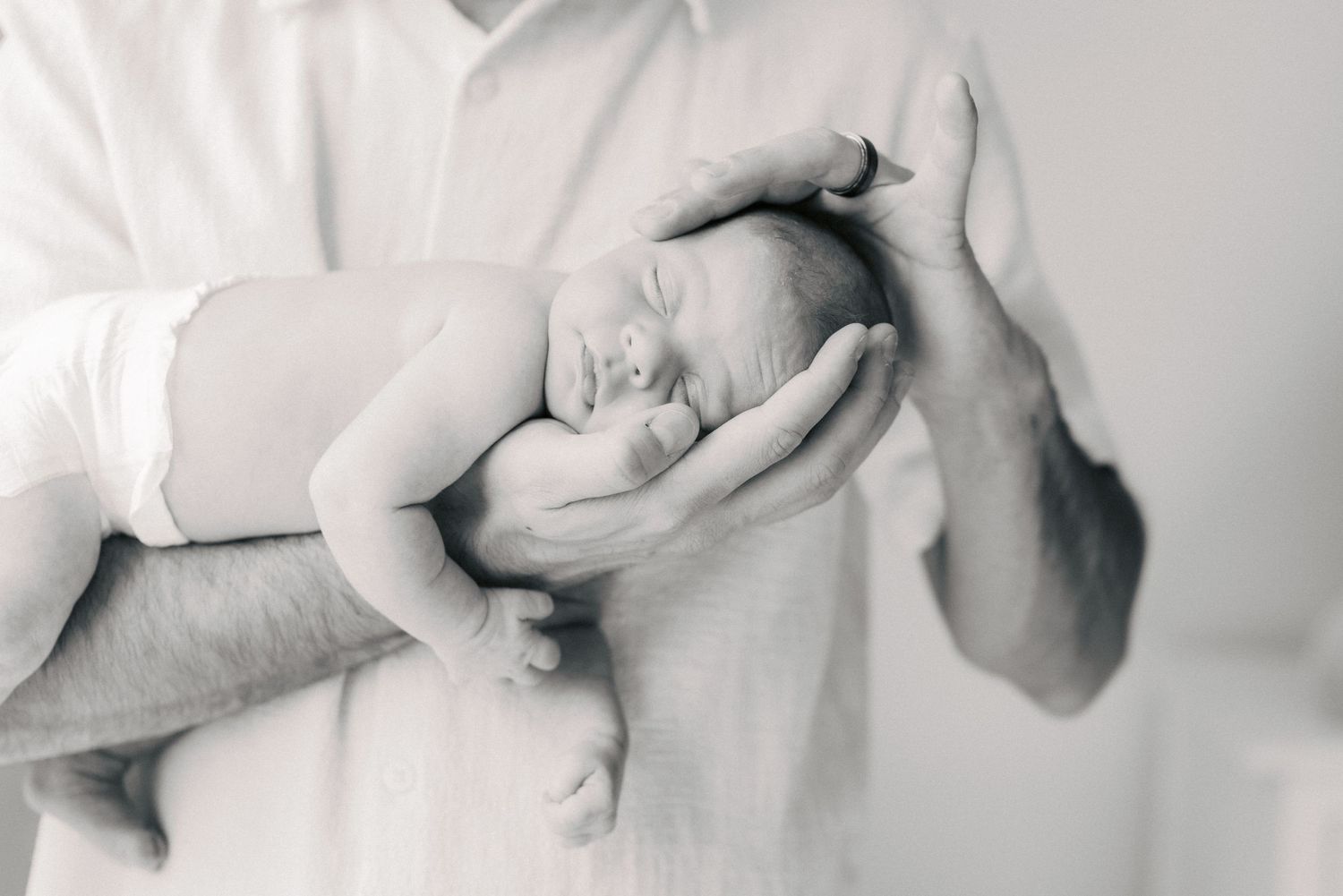 Black and white photo of a newborn baby sleeping peacefully in fathers hands.
