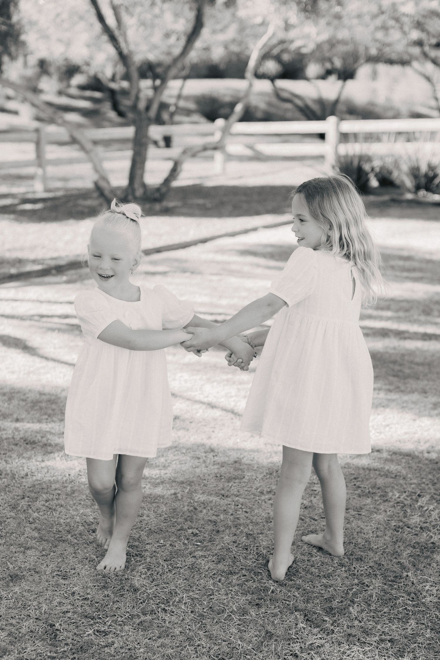 Two young sisters in white dresses holding hands and playing in park, black and white.