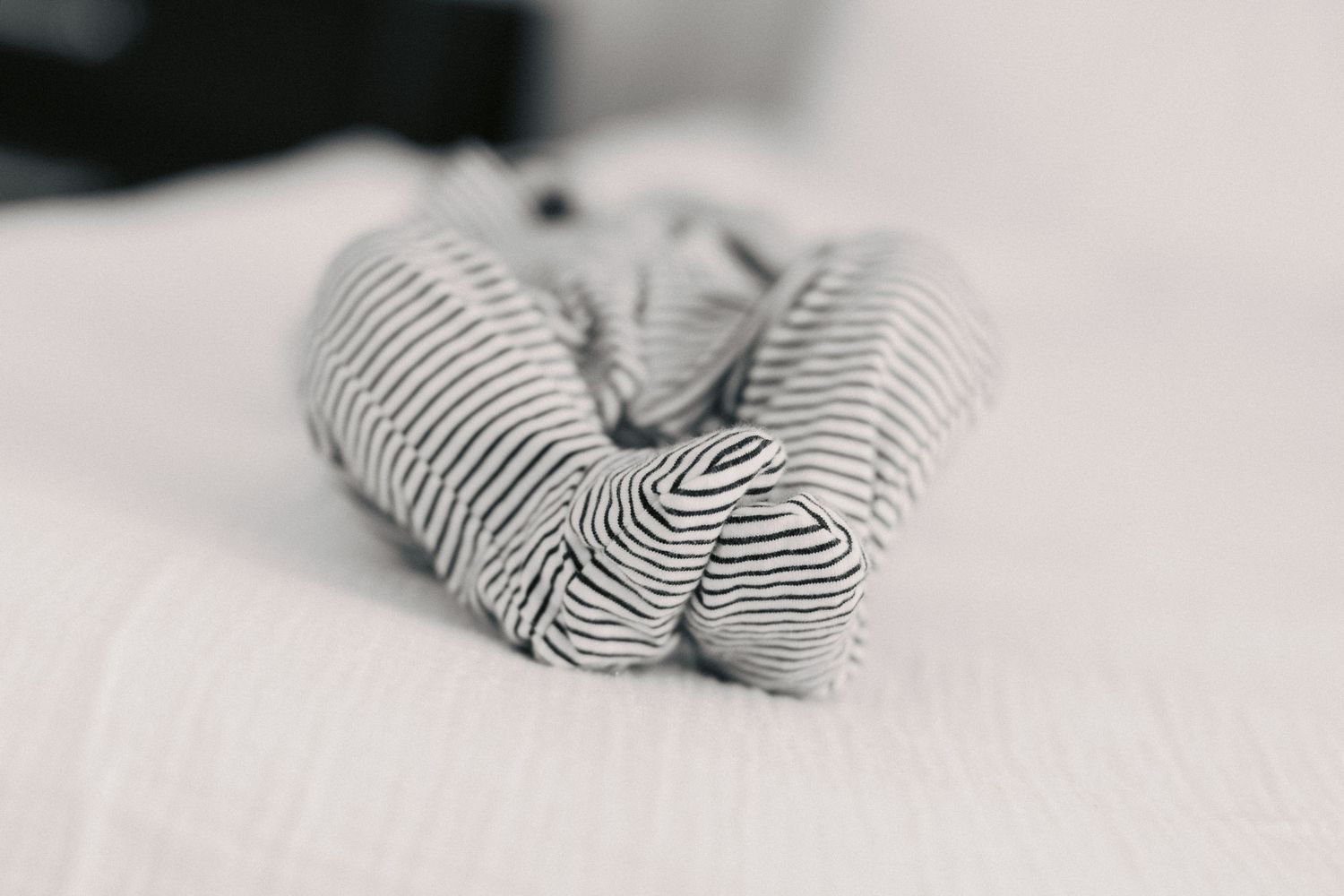 A neatly rolled striped gray and white fabric scarf resting on a soft white surface.