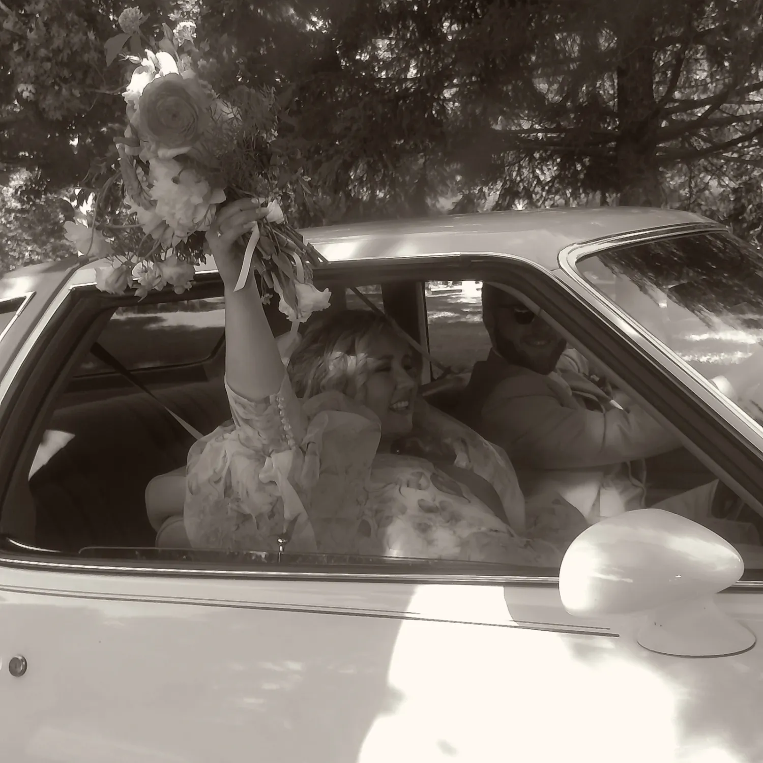 Wedding couple sitting in a classic car captured in black and white photography.