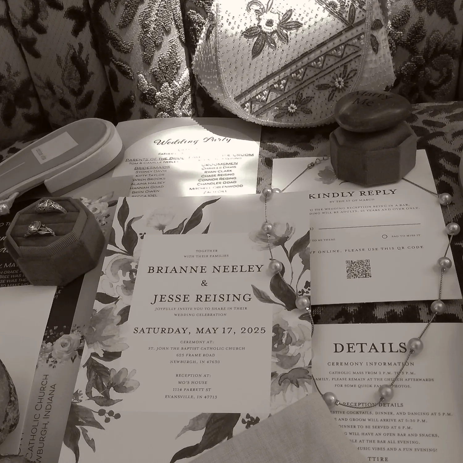 Black and white photograph of wedding invitation suite with floral details and multiple paper cards laid out on patterned fabric.
