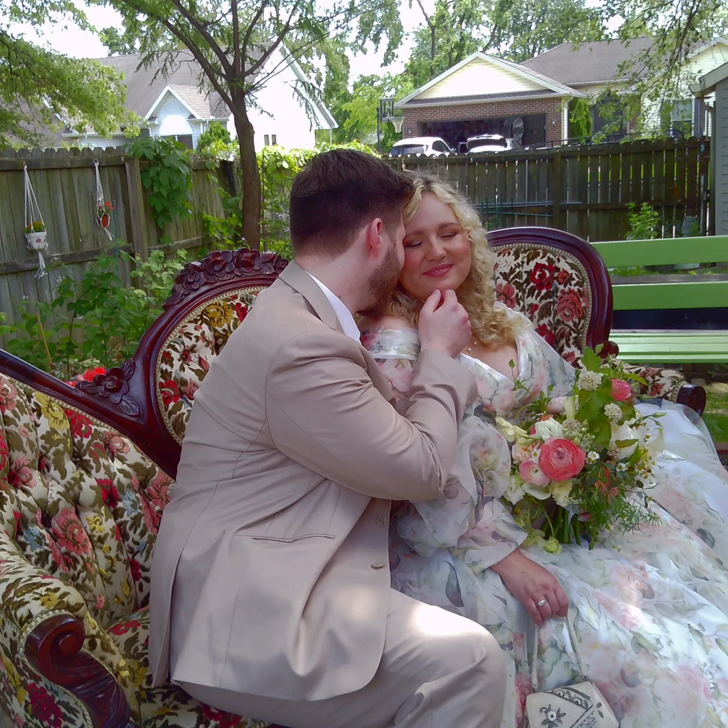 A couple shares romantic moments on a garden bench surrounded by lush greenery and floral arrangements.