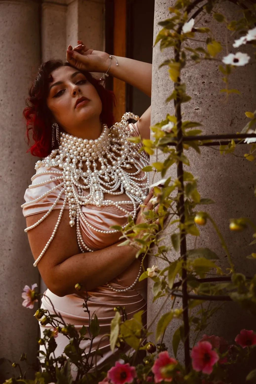 Elegant pearl necklace and body jewelry displayed against floral garden backdrop in romantic boudoir setting.