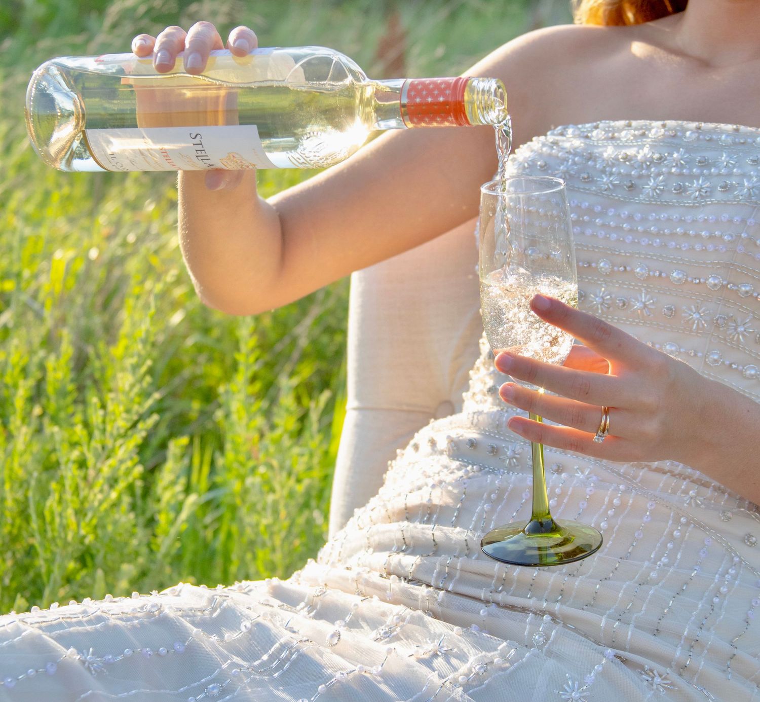 A person's hands gently hold a delicate white lace wedding dress fabric against a sunlit outdoor background.