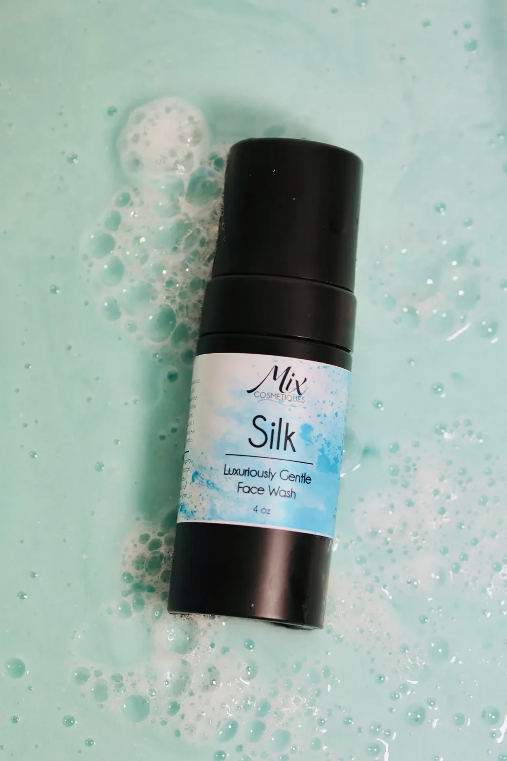 Black cosmetic jar with 'Silk' label sits on a mint green speckled surface in four different angles.