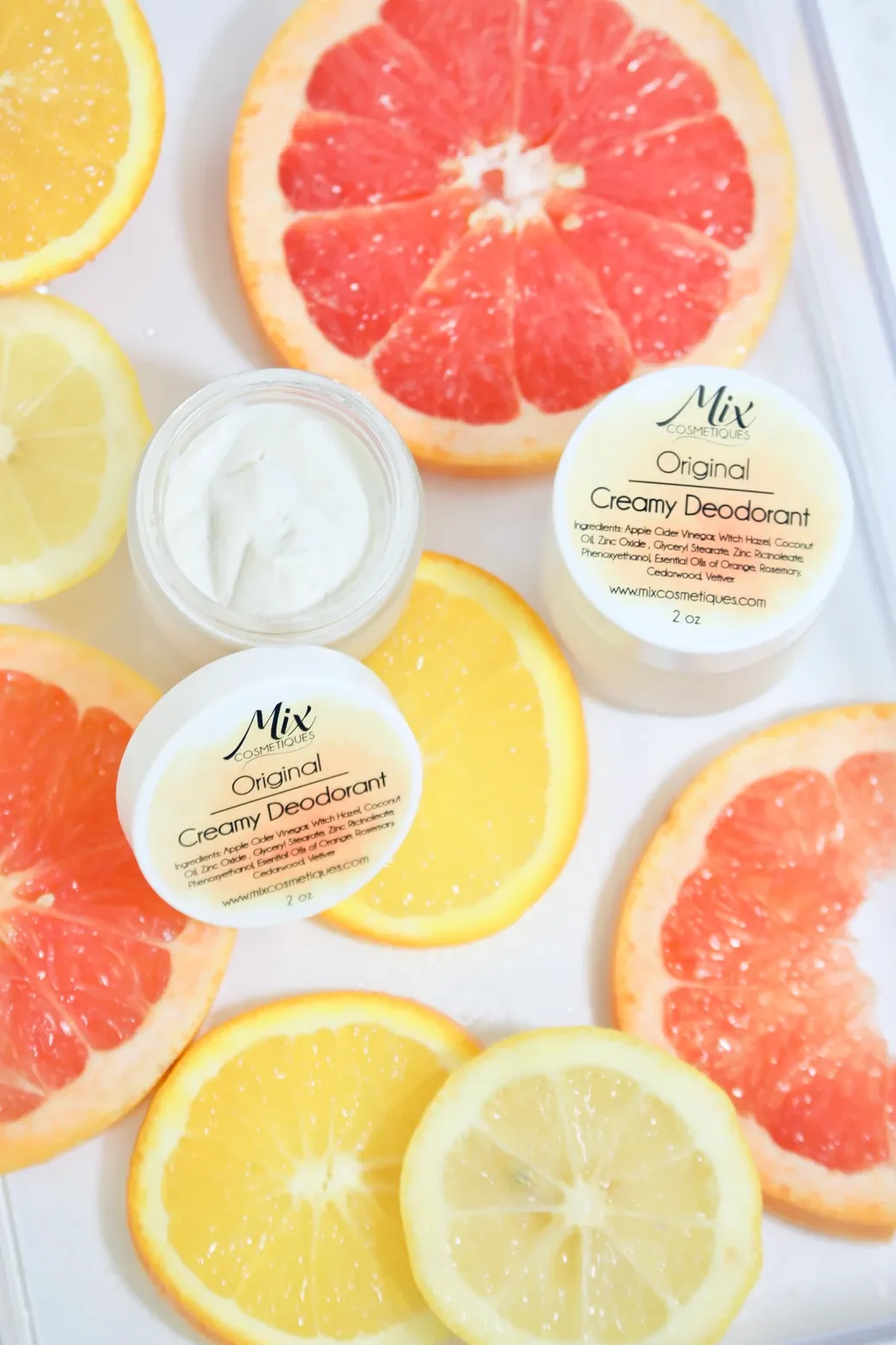 Citrus slices of grapefruit and lemon arranged with organic deodorant products on white background.
