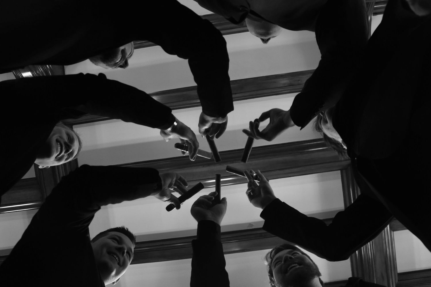 Black and white overhead shot of hands reaching toward center in circular formation.