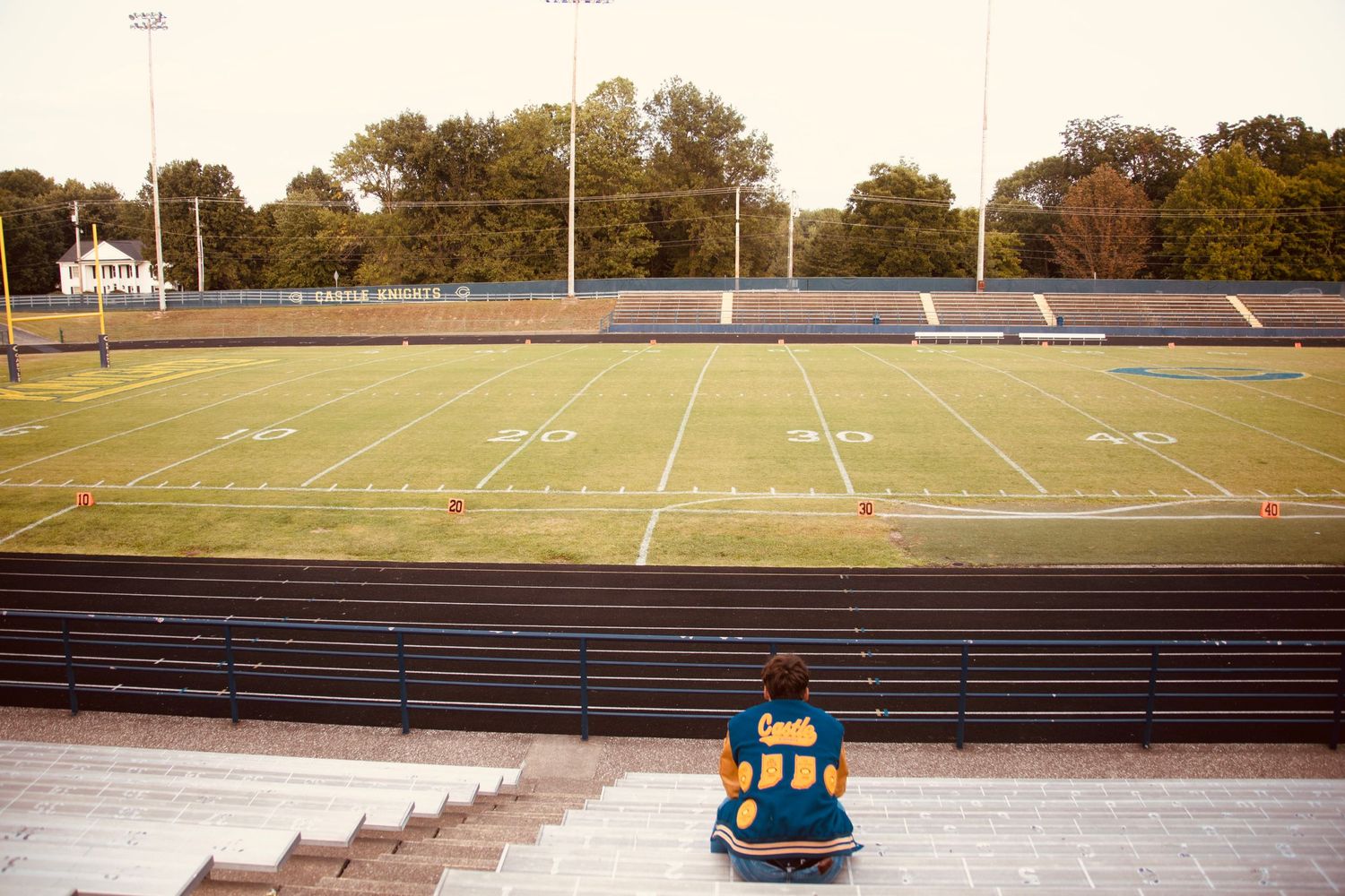 Empty stadium bleachers and football field with goal posts and yard lines visible at sunset.