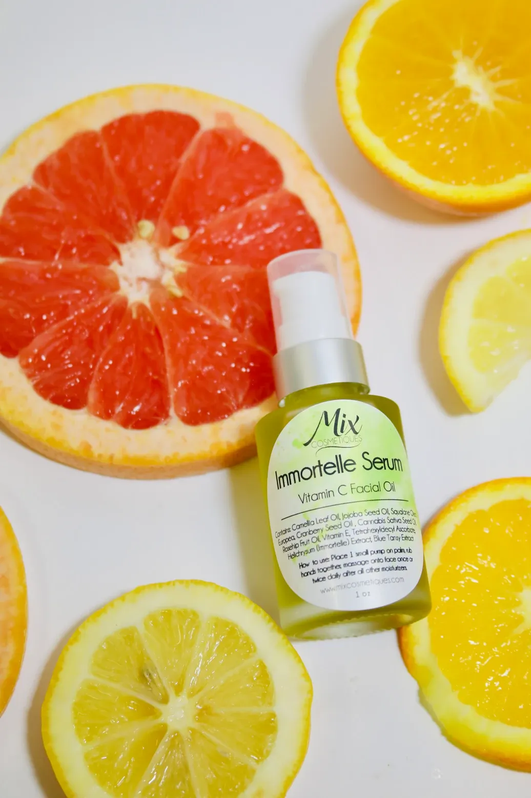 A green bottle of lemonelle serum surrounded by fresh citrus slices including grapefruit, lemon and orange.