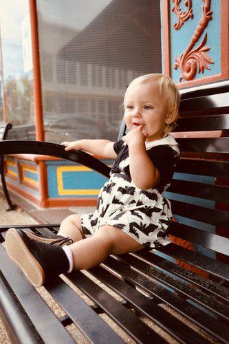 Small child in black and white outfit playing on wooden bench.