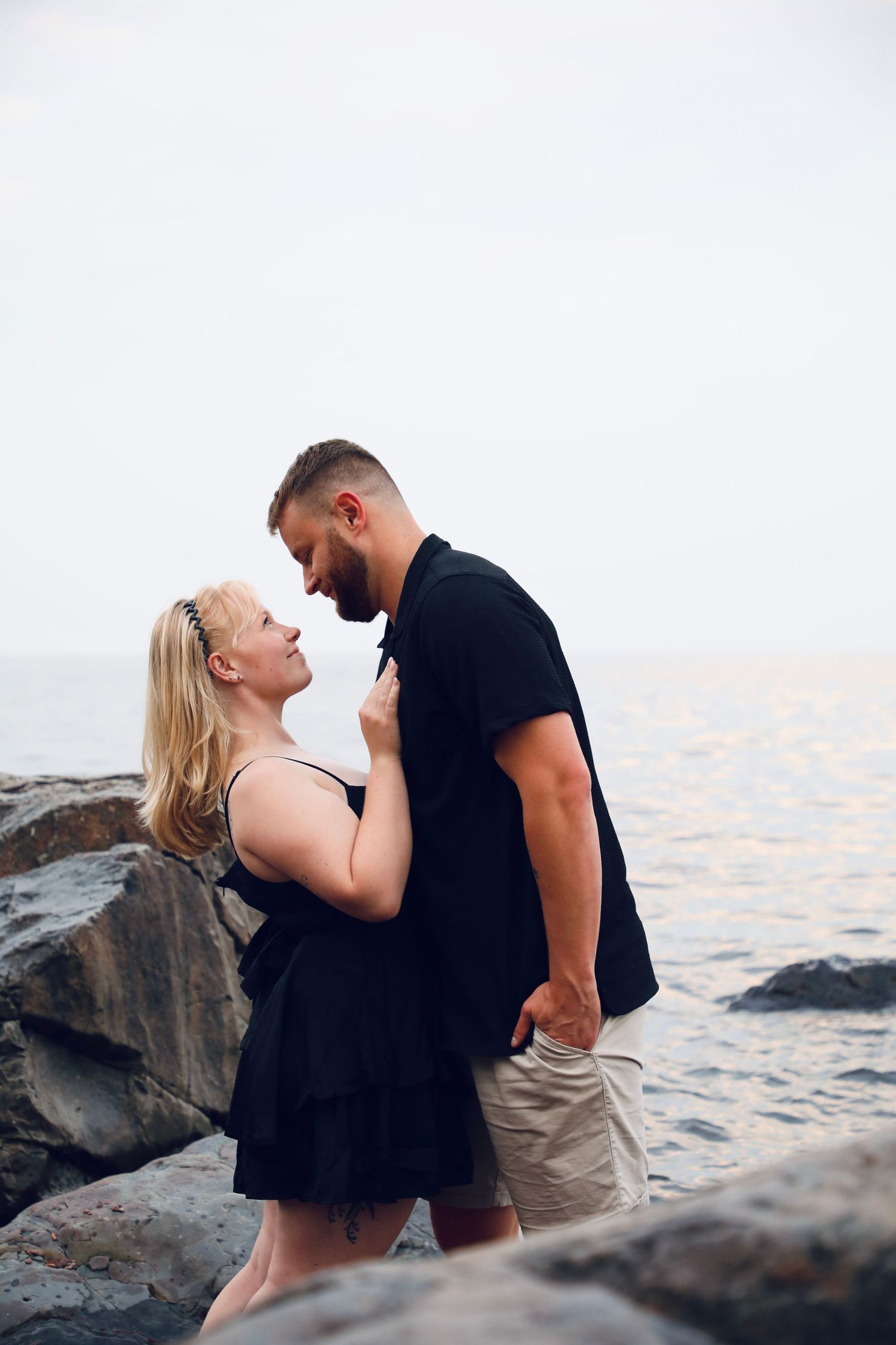 Romantic couple embracing on rocky beach at sunset.