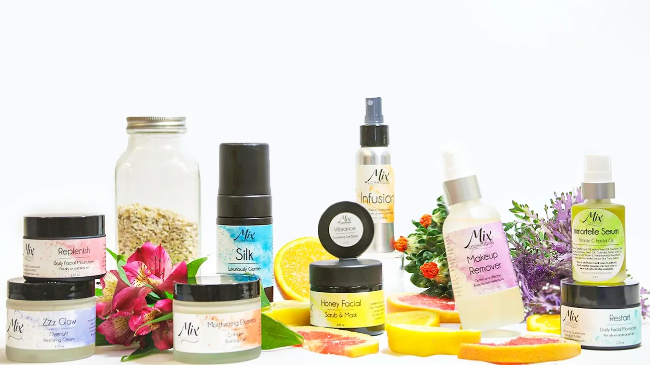 A row of natural skincare and beauty products with colorful flowers and citrus fruits arranged on a white background.