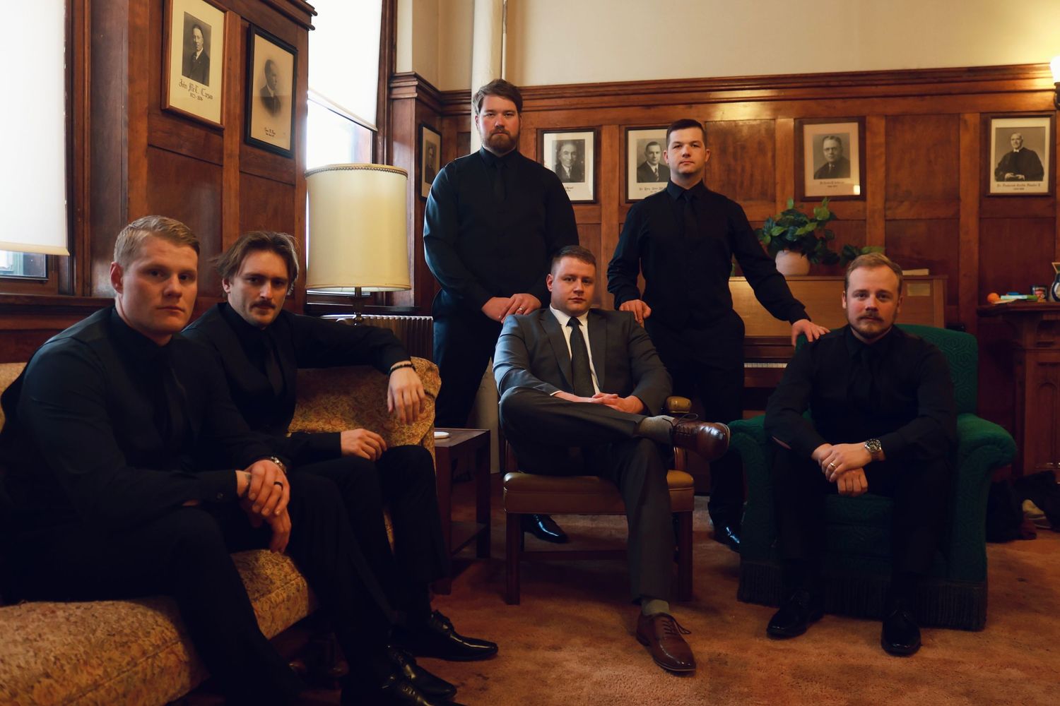 Group portrait in wood-paneled room with vintage photographs on walls.