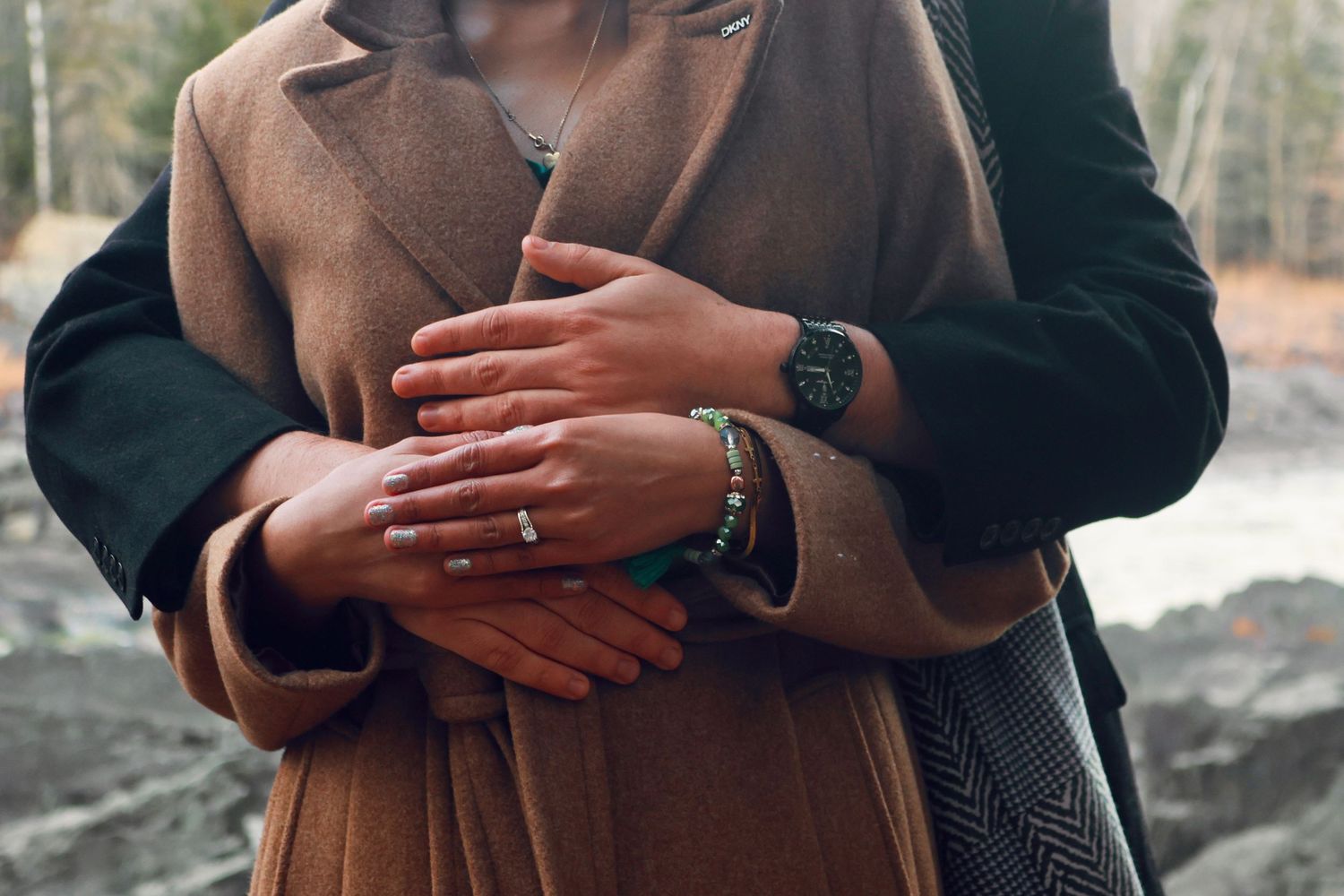 Close-up shot of embracing couple showing rings and winter attire.