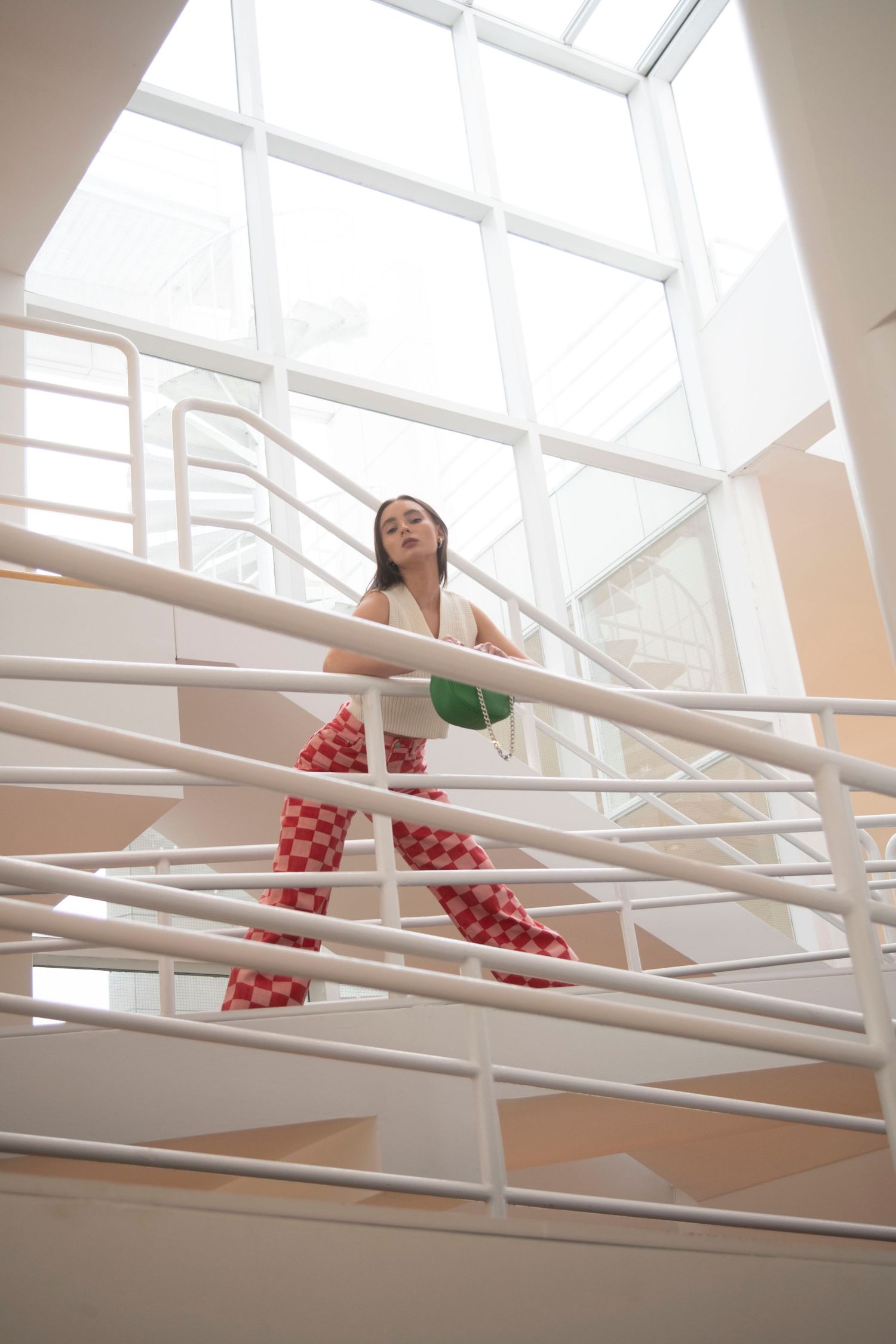 A figure in white reaches through geometric white beams in a bright, modern architectural space with natural lighting.