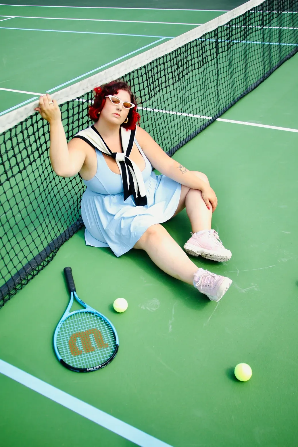 A tennis player rests on a green court with a racquet and tennis ball beside the net.