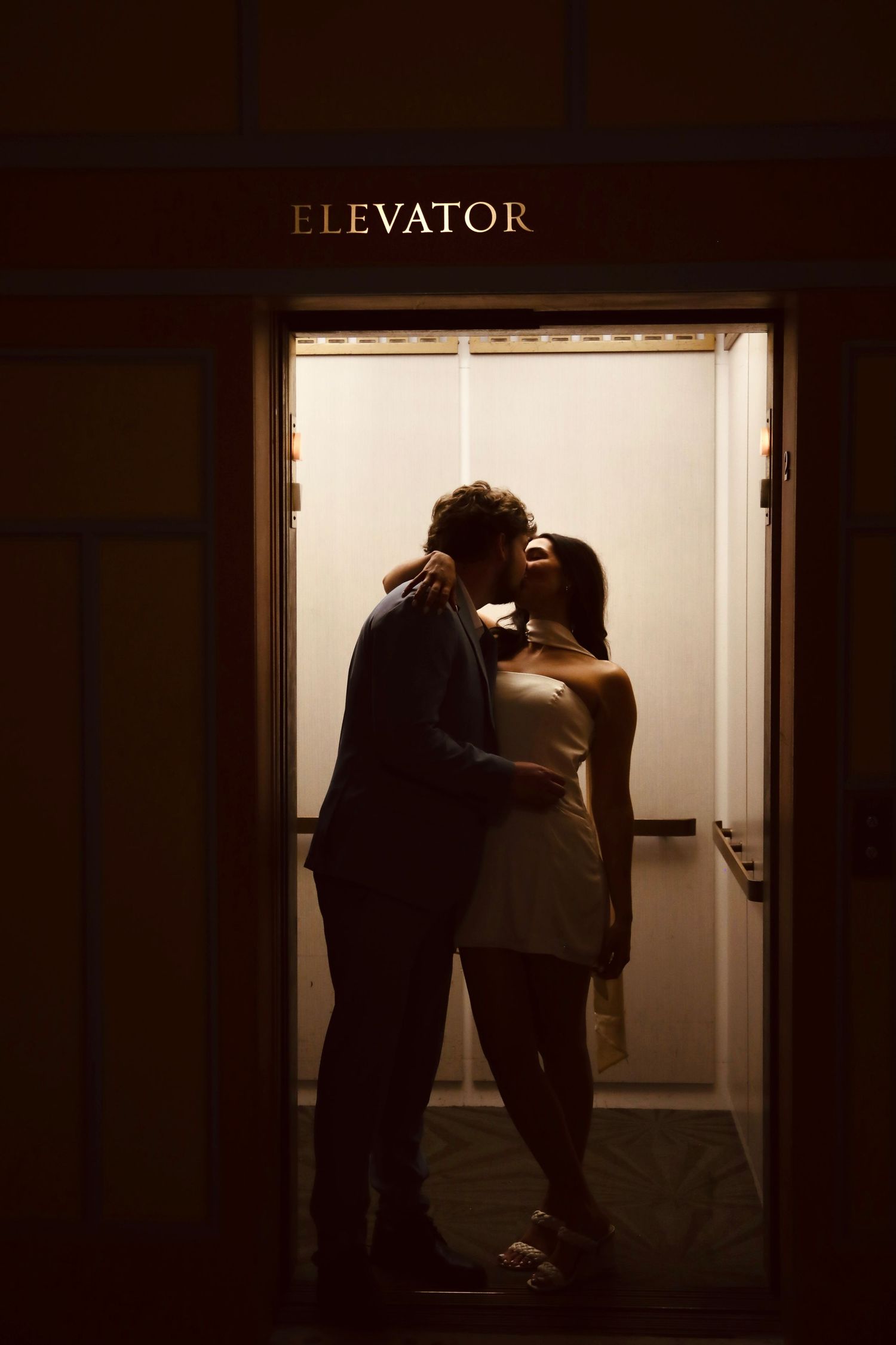 Silhouetted figures embracing in front of an illuminated elevator entrance.