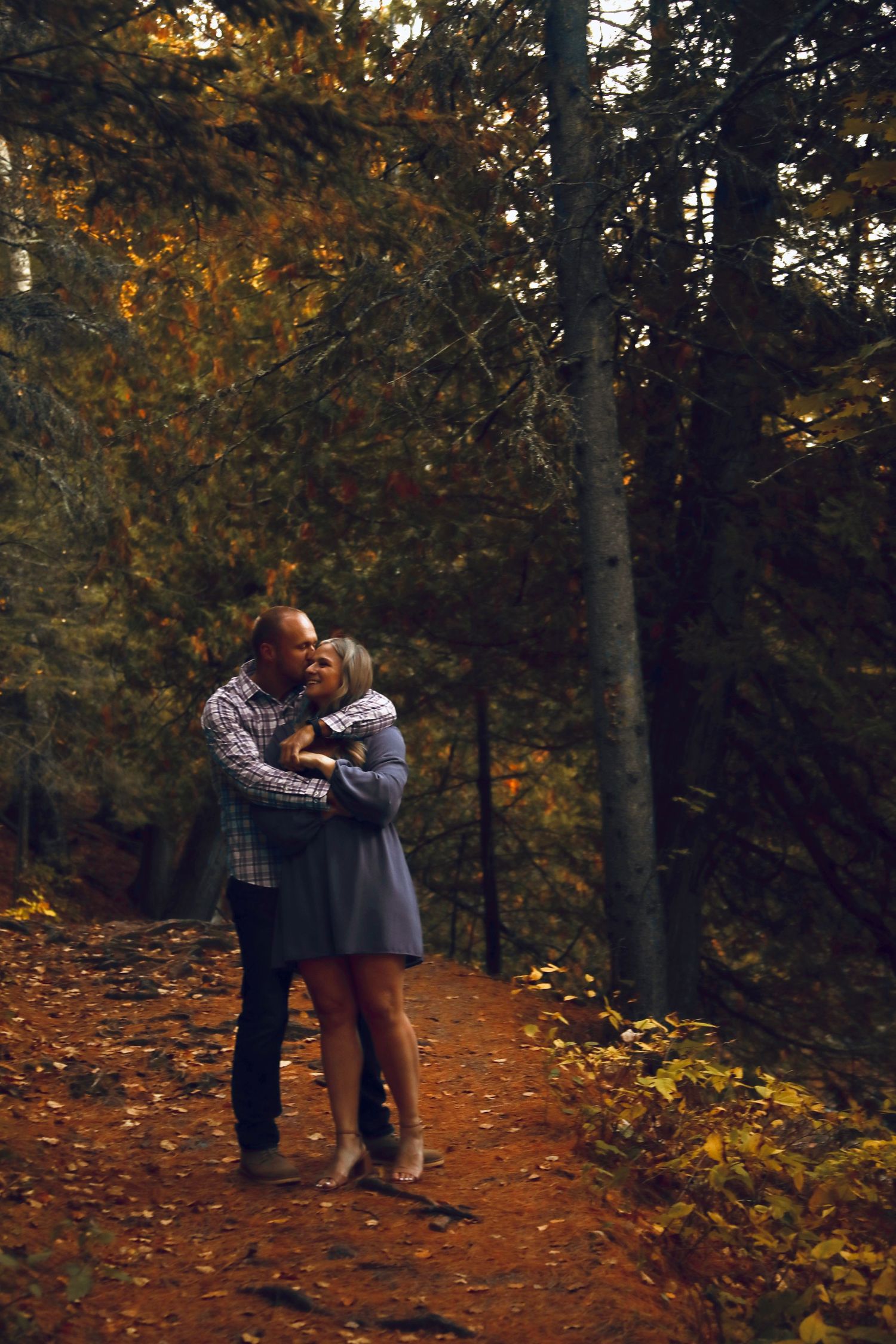 A romantic couple shares tender moments on a leaf-covered forest path during autumn.