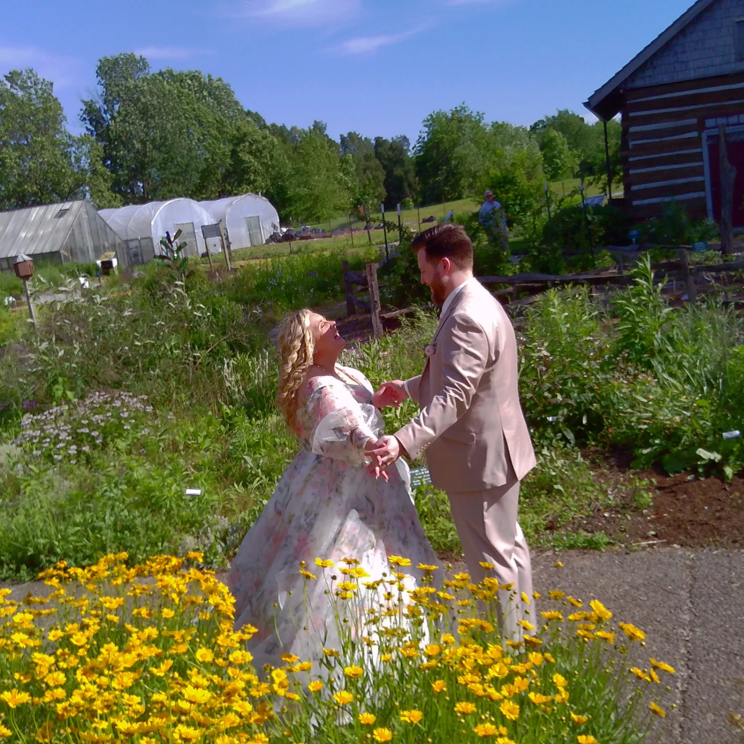 Two people in flowing dresses dance together in a garden filled with vibrant yellow and white wildflowers.