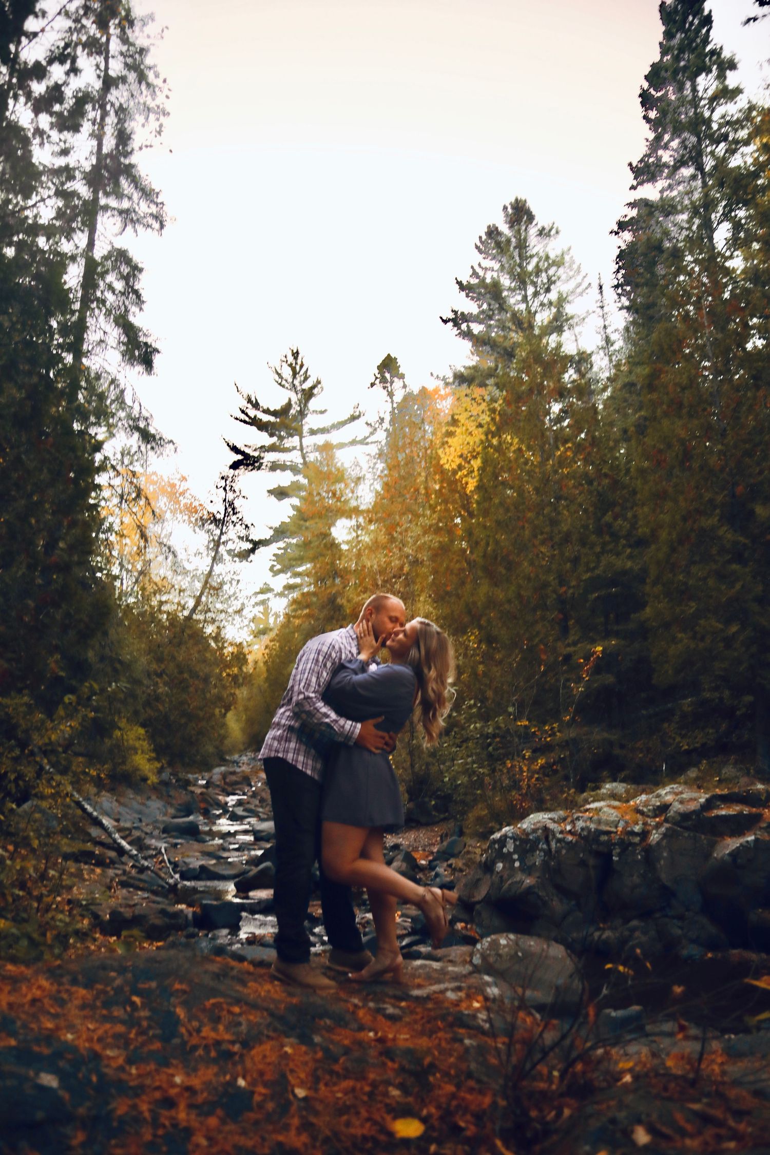 A couple shares a romantic moment on rocky terrain near a stream during golden hour.