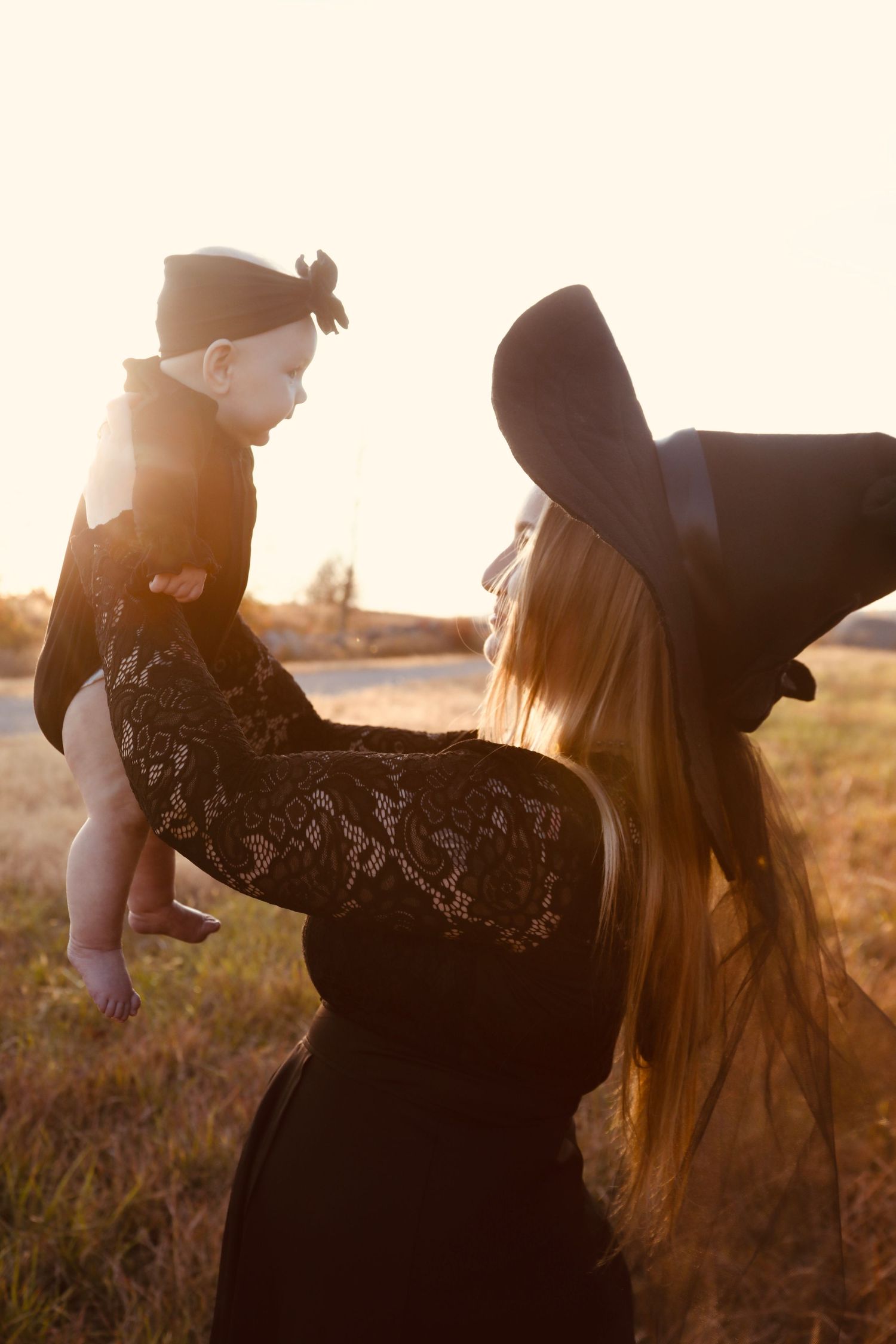 Silhouette figures in black clothing against golden sunset in field.