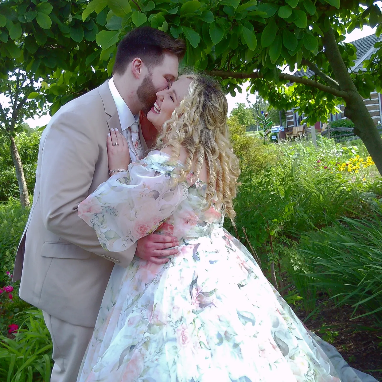 A romantic couple in formal attire share intimate moments in a lush garden setting with green foliage.