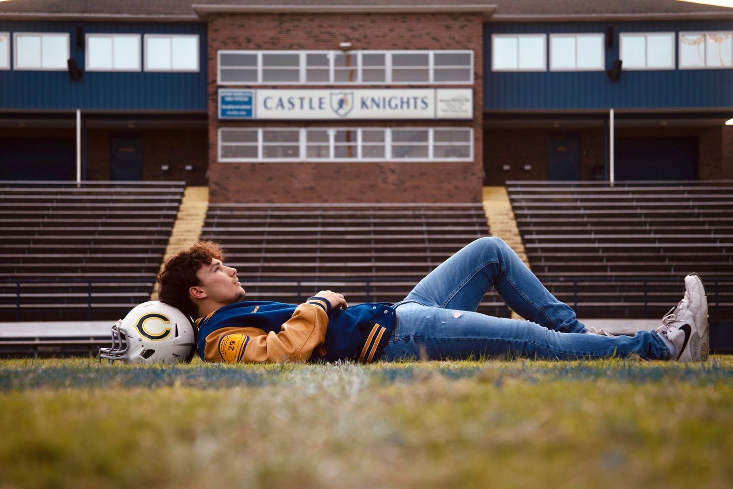 A person lies on a bench at a sports field during golden hour.
