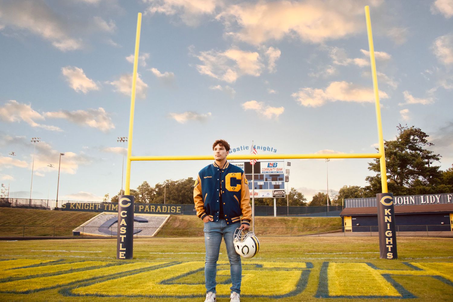 Football field goal posts cast long shadows across an empty stadium field at sunset.