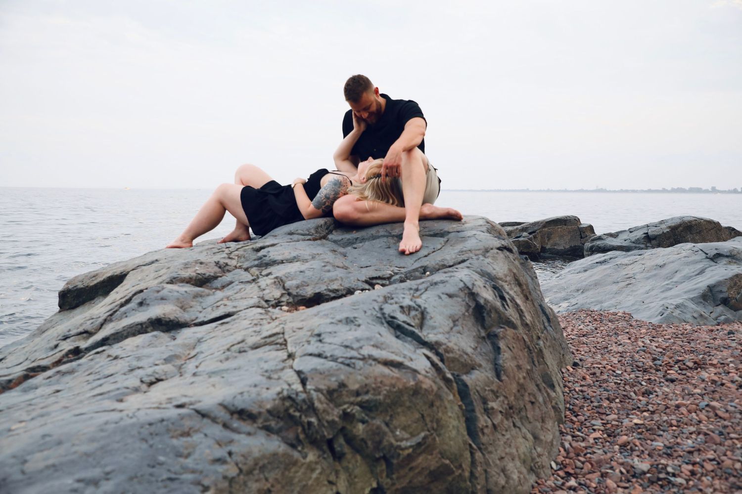 Couple lounging on rocky shoreline during sunset photoshoot.