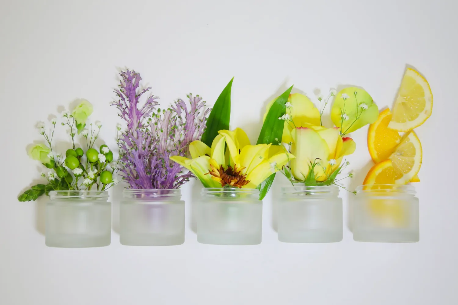 Frosted glass tumblers filled with colorful cocktails garnished with fresh citrus slices, herbs and purple flowers.