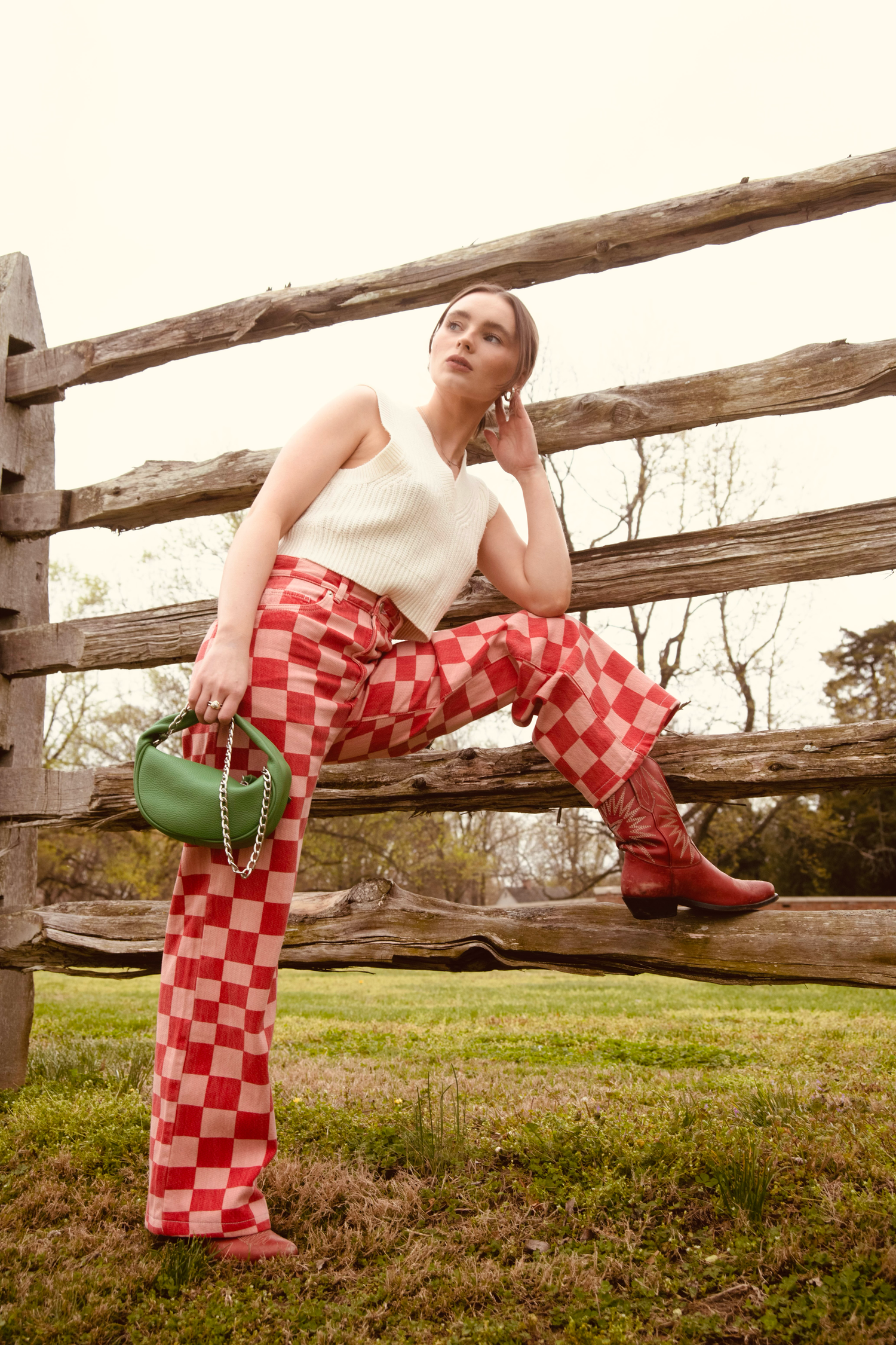 Red checkered dress and green boots posed artistically along wooden fence in nature.