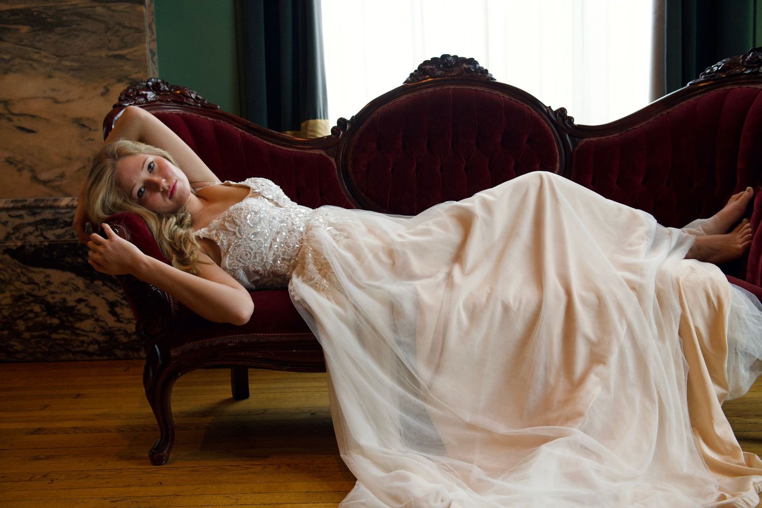 Bride in white gown lounges elegantly on vintage furniture.