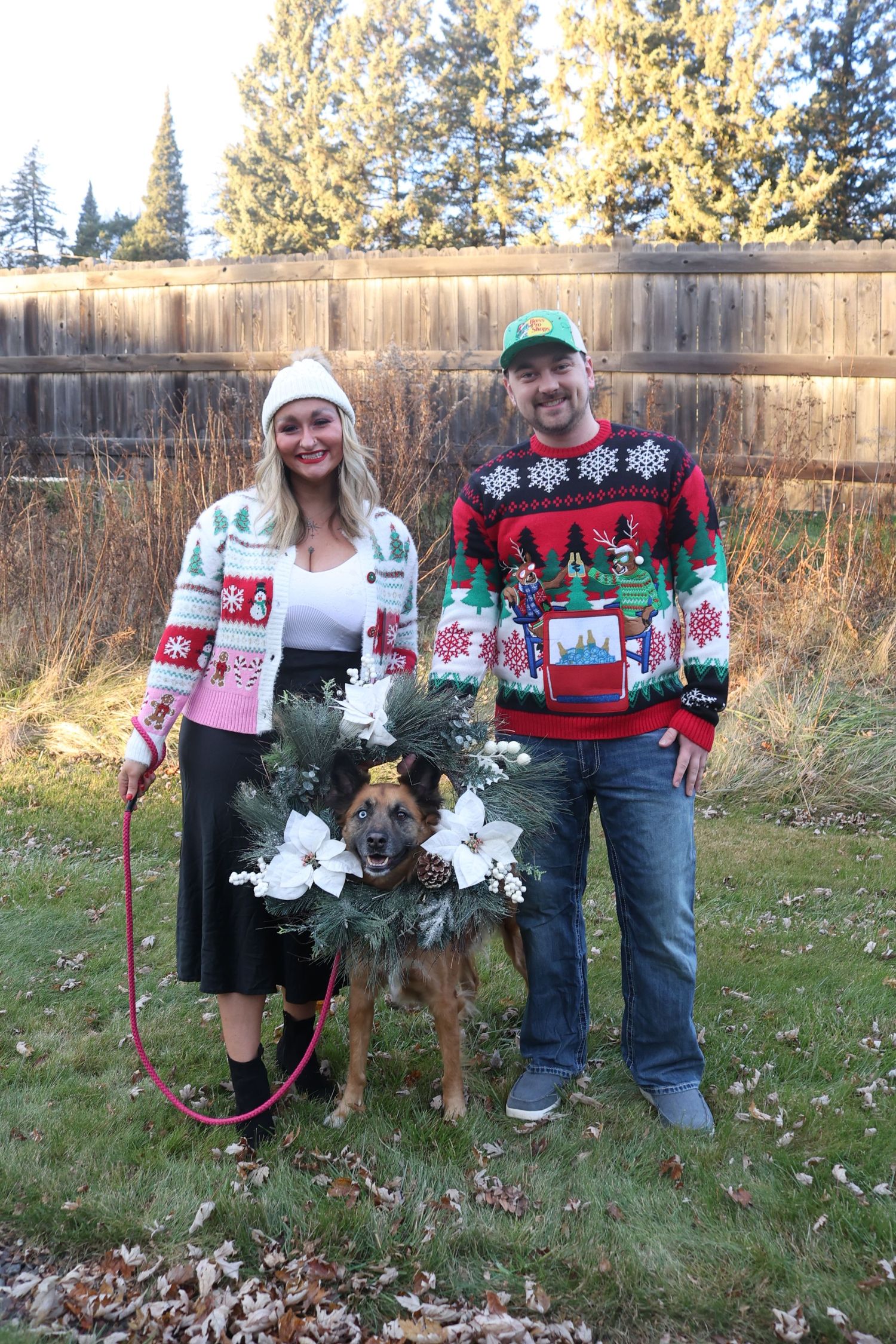 Group wearing festive Christmas sweaters posing with holiday decorations in a backyard.