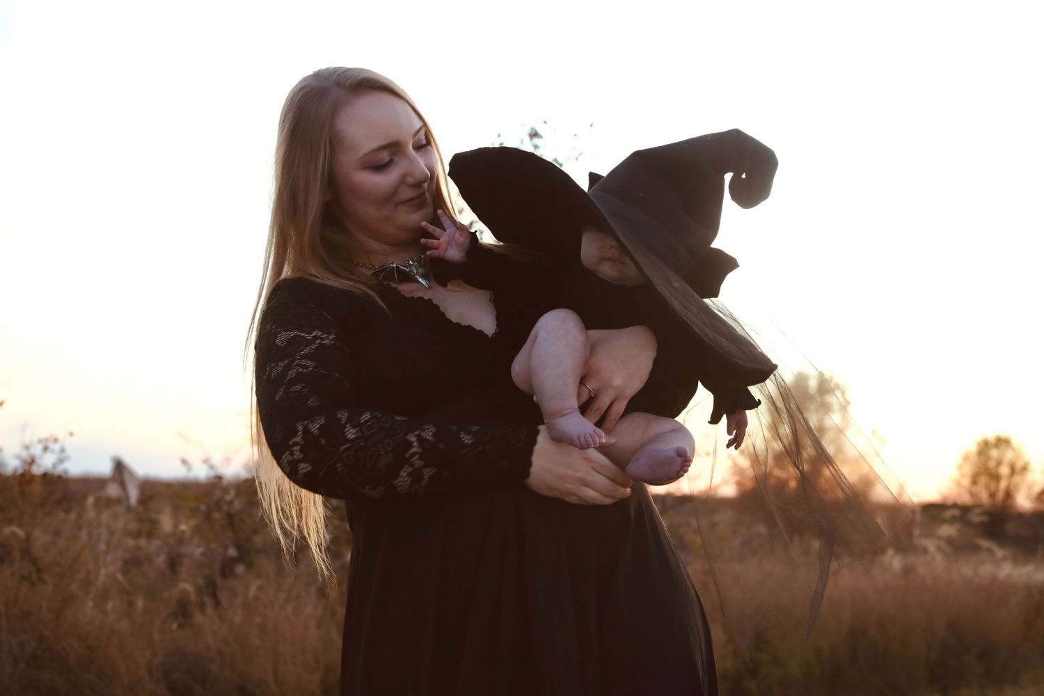 Figure in black dress and hat standing in field at sunset.