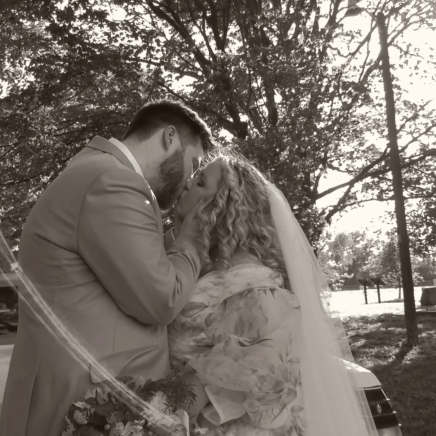 Newlyweds share a romantic moment outdoors in a black and white photograph.