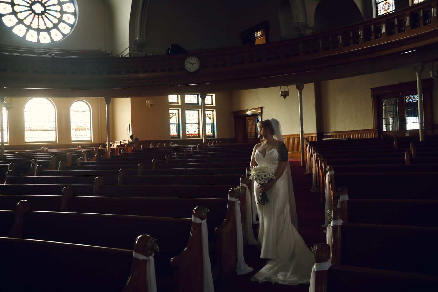 Interior view of a historic church sanctuary with dark wooden pews and natural light streaming through windows.