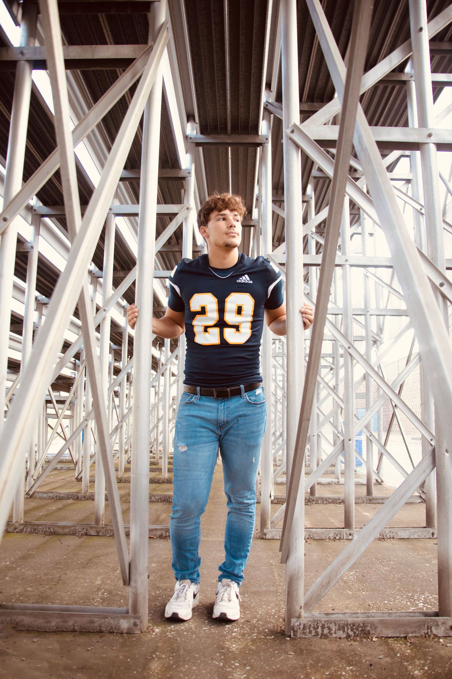 Athletic figure in navy jersey number 29 and blue jeans poses between white structural beams under stadium.